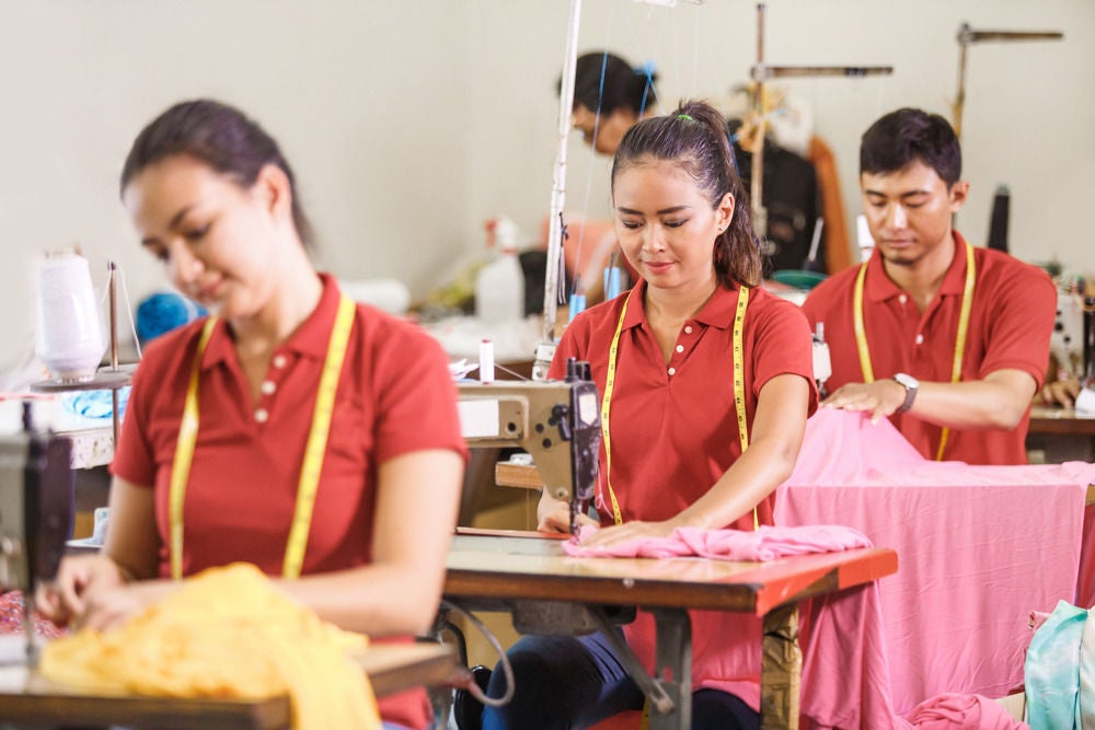 A group of manicurists wearing face masks and red aprons attending to customers.